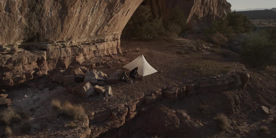 A person below is setting up a tent near a cavern