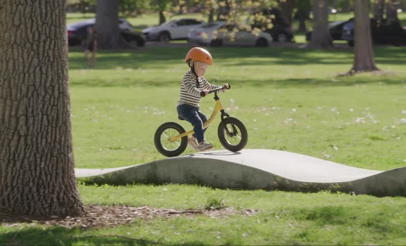 Little boy riding a bicycle with a helmet on a raised track in a grassy park
