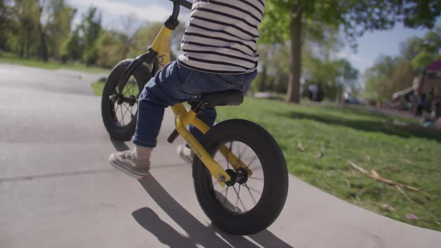 A child is on a yellow bicycle going down a small concrete ramp