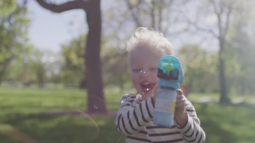 A young boy runs with a water gun in a park on a spring day