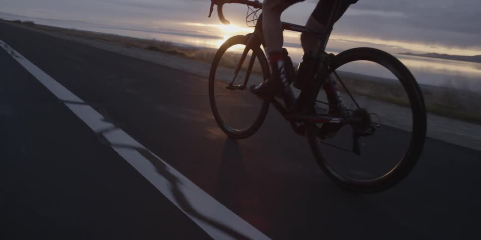 Bicyclist pedaling beside the roadway at sunset on a cloudy evening