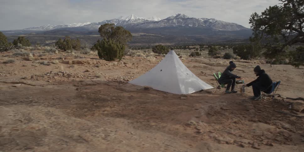 Passing view of two campers sitting on their chairs outside of their tent