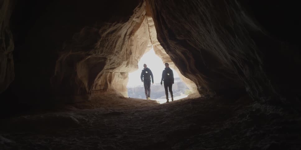 Couple walking into a cave like area with their lights hanging from their chests