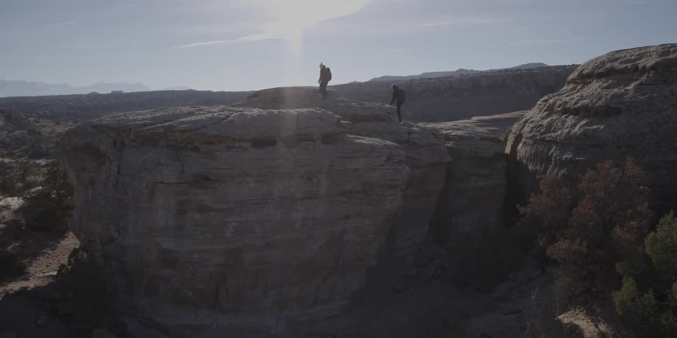 Two people hike to the top of a rocky ridge and wander around the top