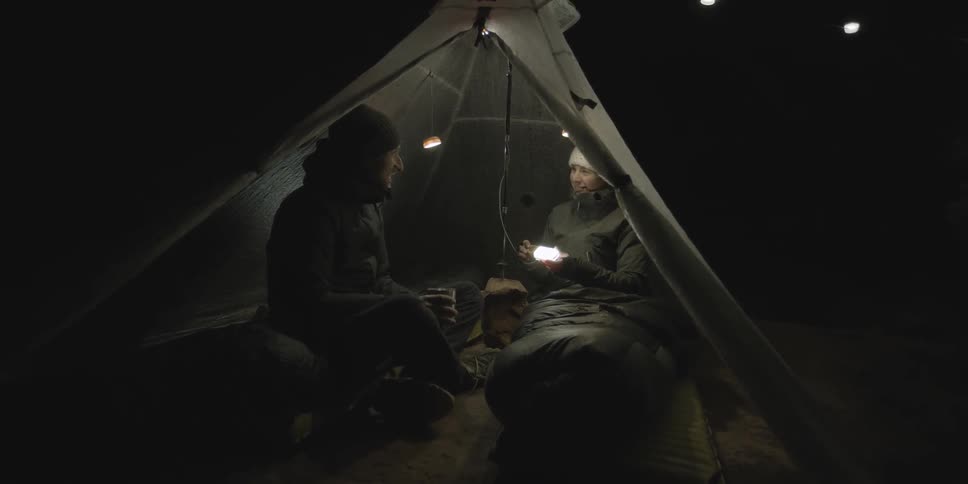 Man and woman sitting in tent at night talking and laughing