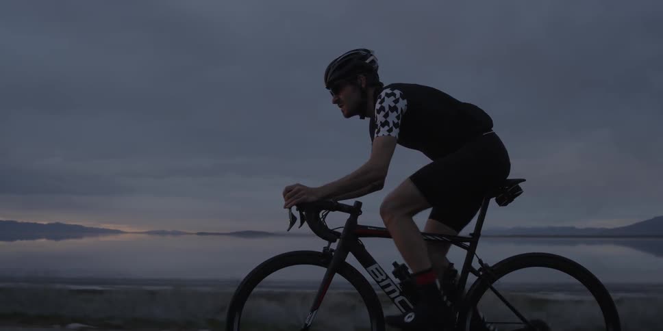 A man is mountain biking near a large lake at sunset