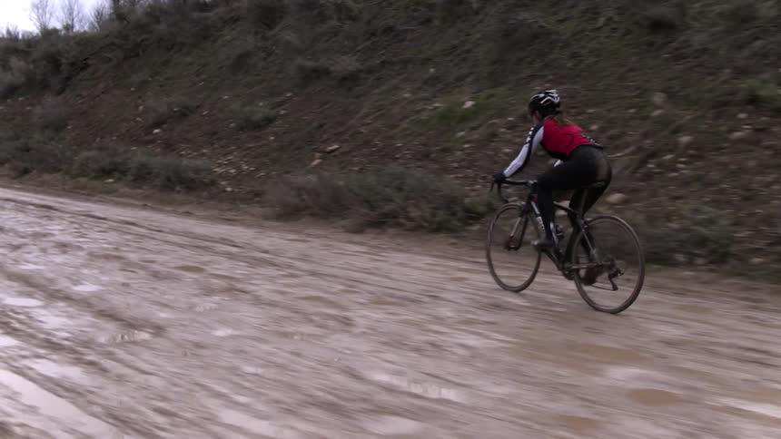 A woman rides a bike down a muddy dirt road