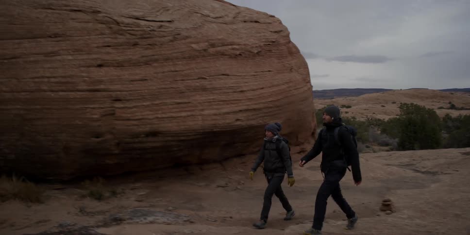Two people hike along a canyon on a cloudy day