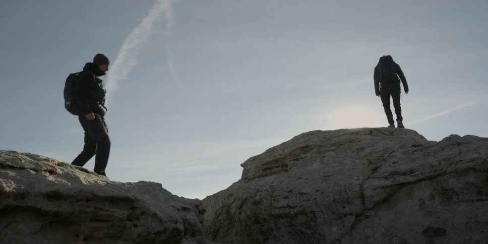 Two hikers jump over a rock crevice