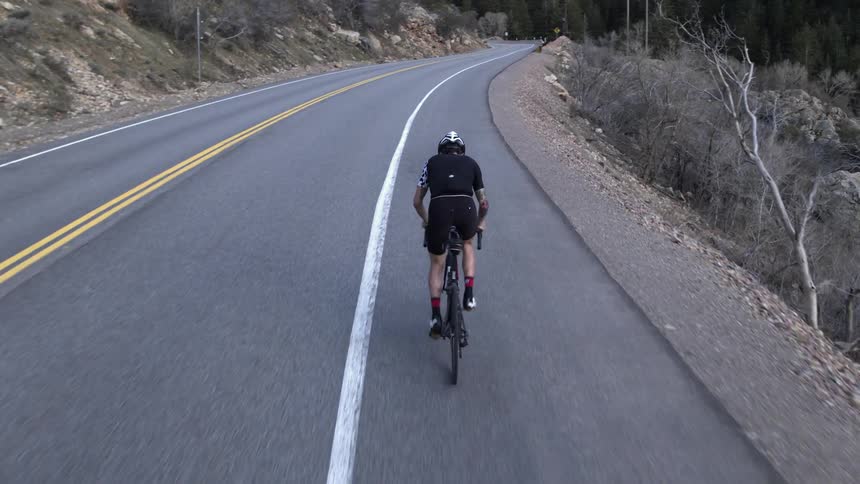 A man rides his bike fast down a road near a hillside