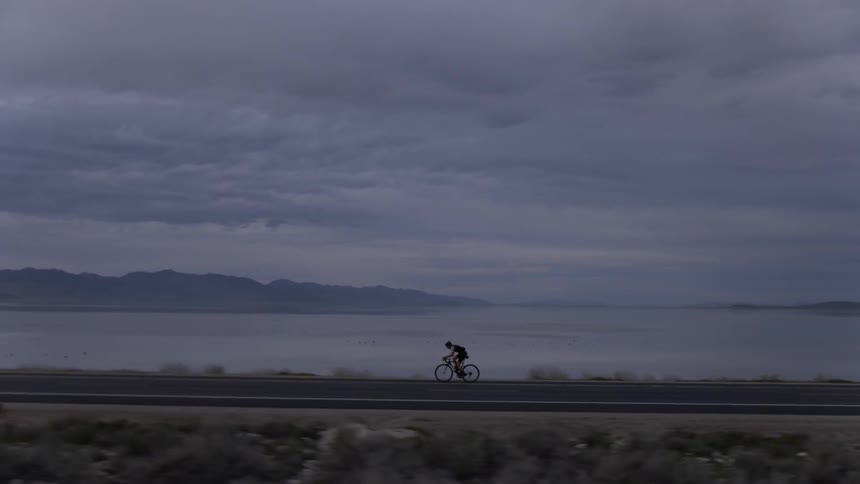 Cyclist riding rapidly on a road next to the sea on a cloudy evening
