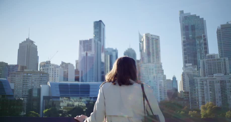 A woman stands on a platform that overlooks a metropolis on an autumn day