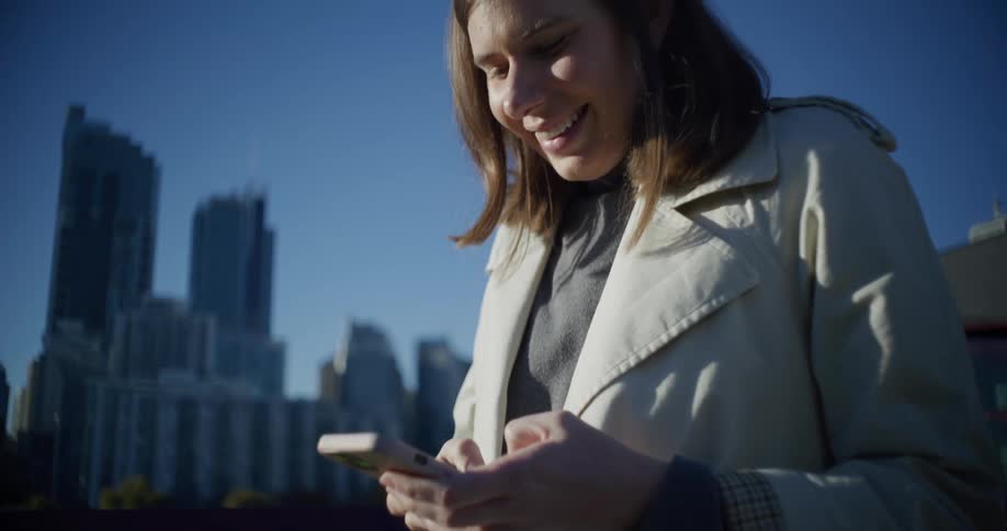 A young woman smiles while texting on her smartphone in a large city