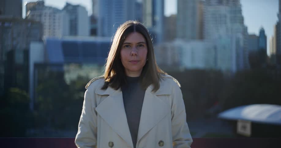 A woman wearing a coat blinks as she stands near a downtown city area
