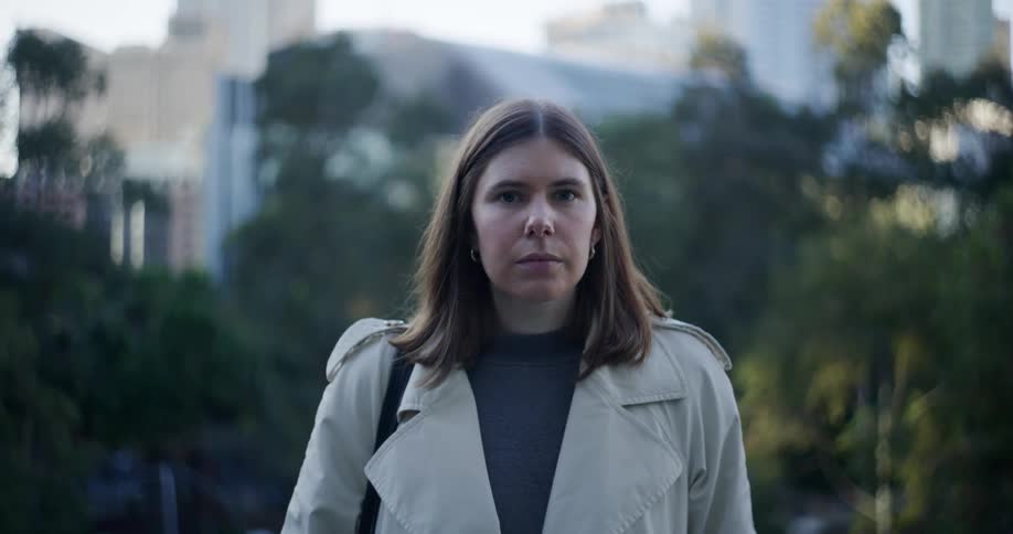 A woman wearing a coat in a city stares into the distance