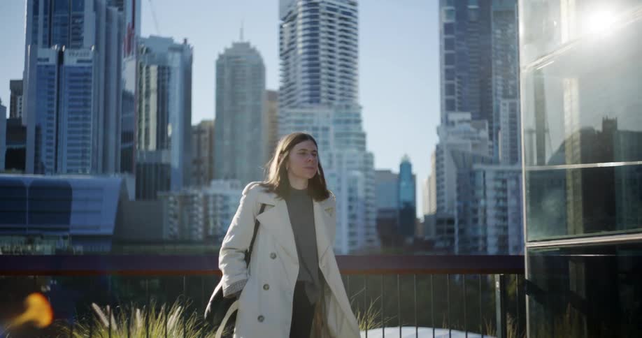 A woman in a white coat is observing the tall buildings of a metropolitan city and then she walks back