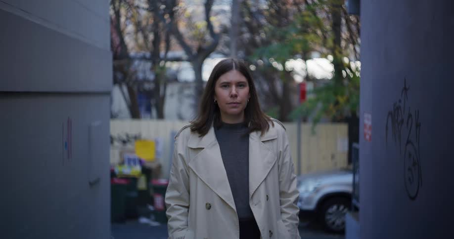 Portrait of a woman wearing a long white coat standing in an alley in the city