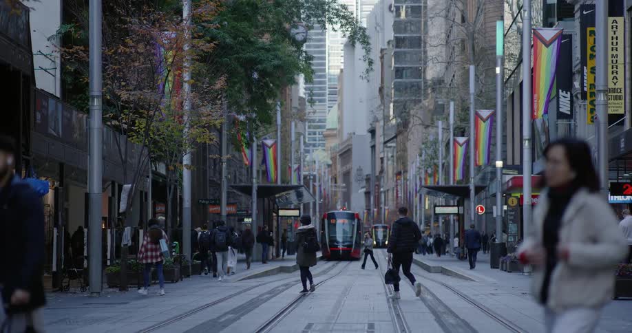 A city street with tram tracks and colorful banners hangs above with people walking along the sidewalks