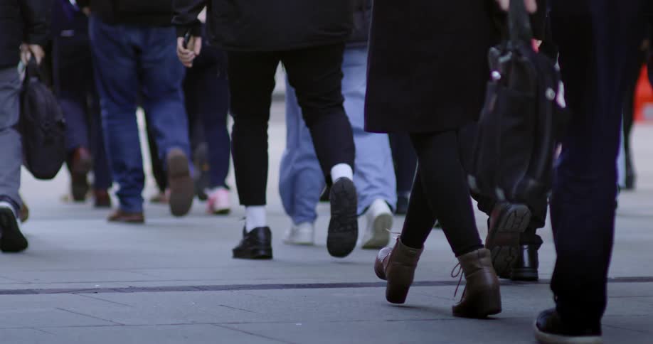 A closeup view of peoples lower legs and feet as they walk on a bustling city street