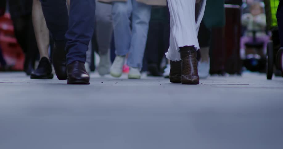 A close up of the lower legs and feet of a person walking on a busy street wearing boots and a white dress