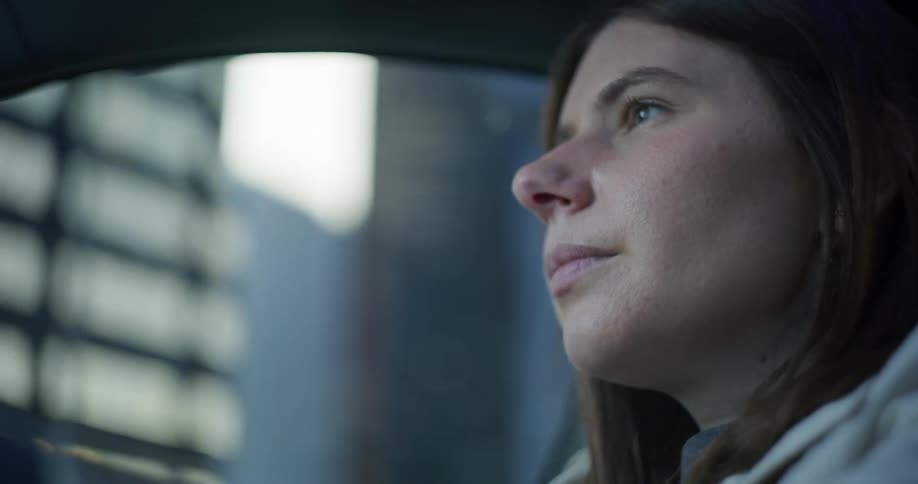 The face of a young woman looking forward and she is inside a car