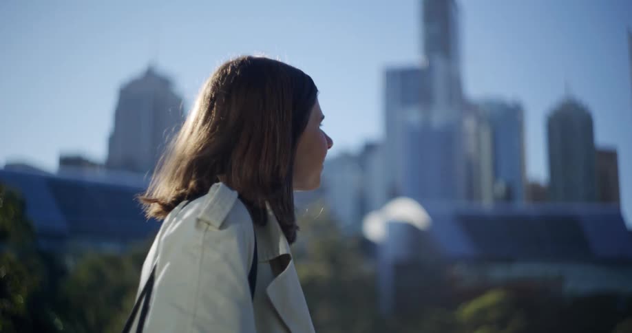 Woman smiles while walking through an urban environment with the city skyline in the background