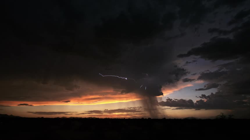 Lightning arcs through dark storm clouds and strikes the ground during a thunderstorm after sunset
