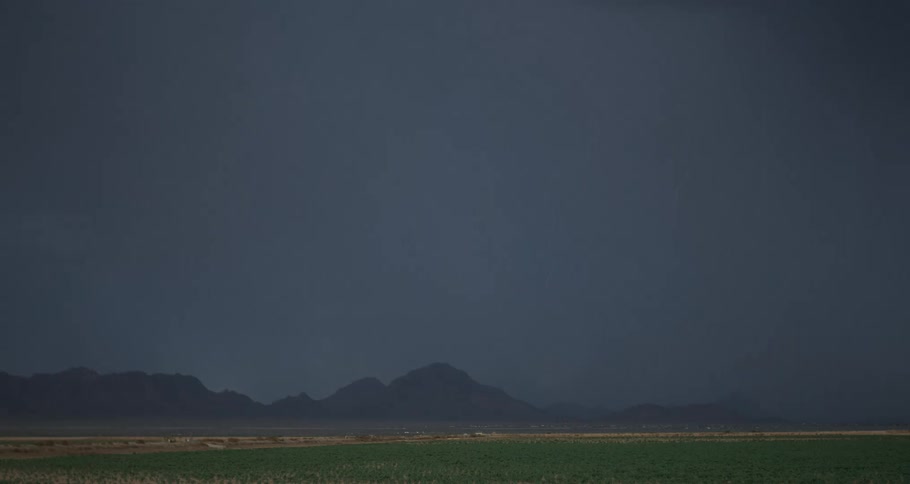 A strong bright ray coming out of a dark cloud in a region with a field and mountains in the background