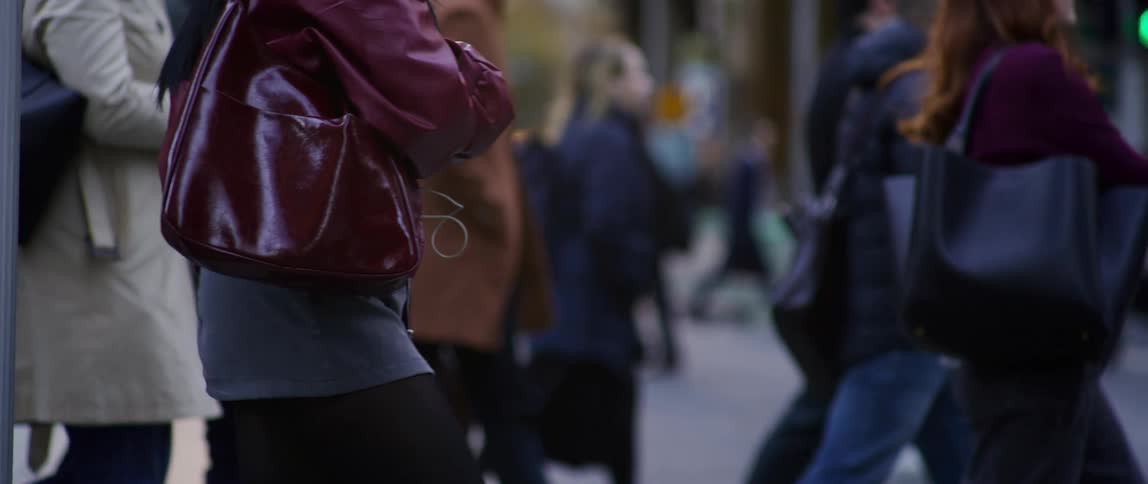 Several people carrying either bags phones or coffee cross a city street