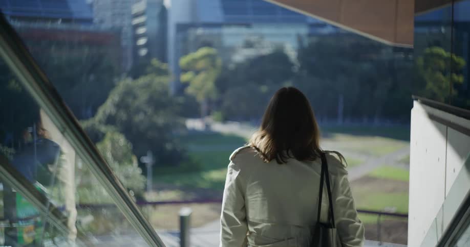 Woman riding an escalator backwards to face the park below her