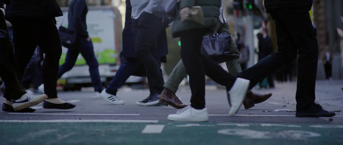 Several legs of people who are crossing an asphalt street at the pedestrian crossing