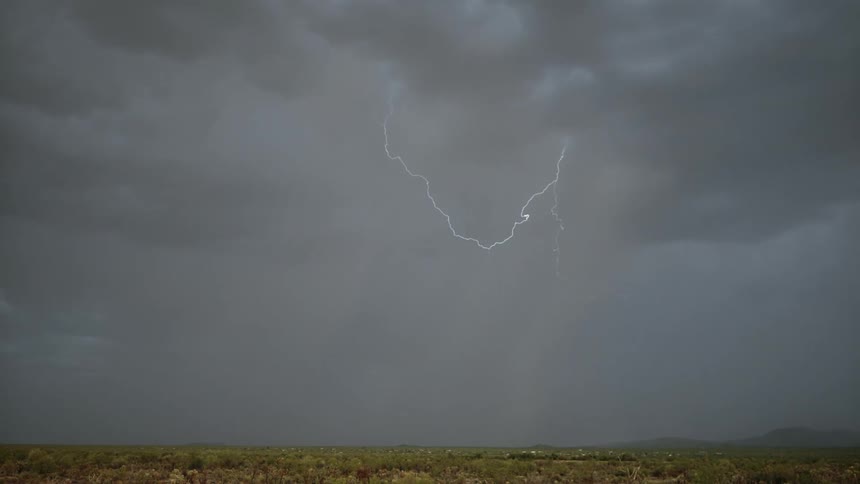 Bright lightning cutting through the gray sky during a thunderstorm with an open plain landscape
