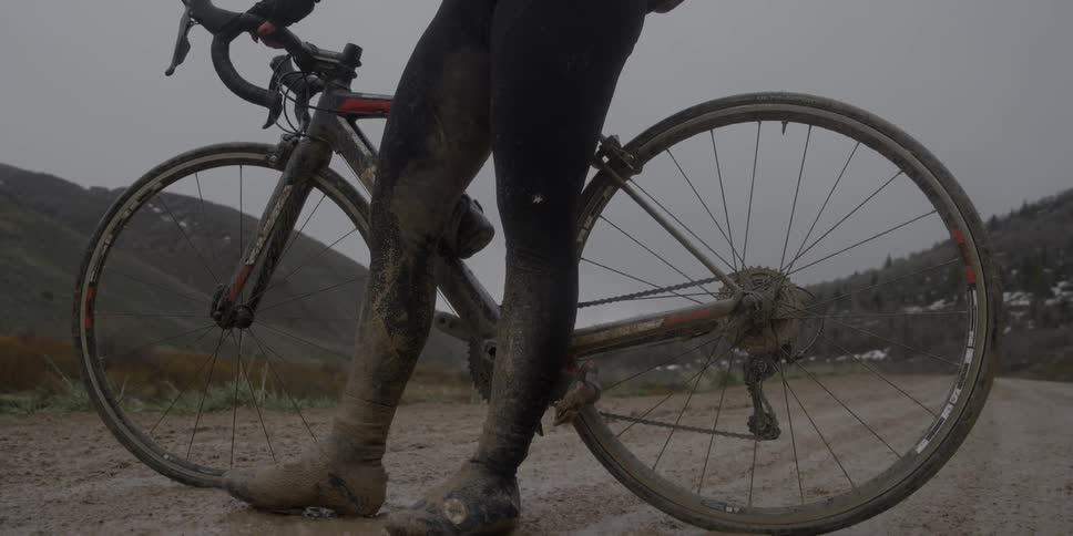 A person with muddy leggings stands beside their bicycle