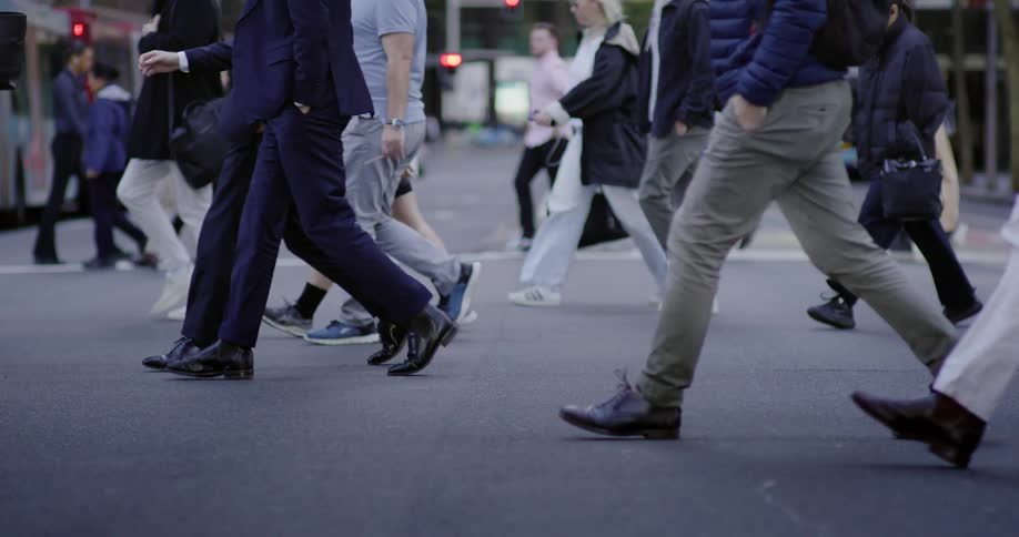 A closeup view of peoples lower legs and feet as they walk on a bustling city street