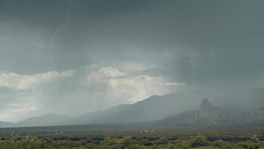 Bright lightning cutting across the sky during a thunderstorm with mountains in the background