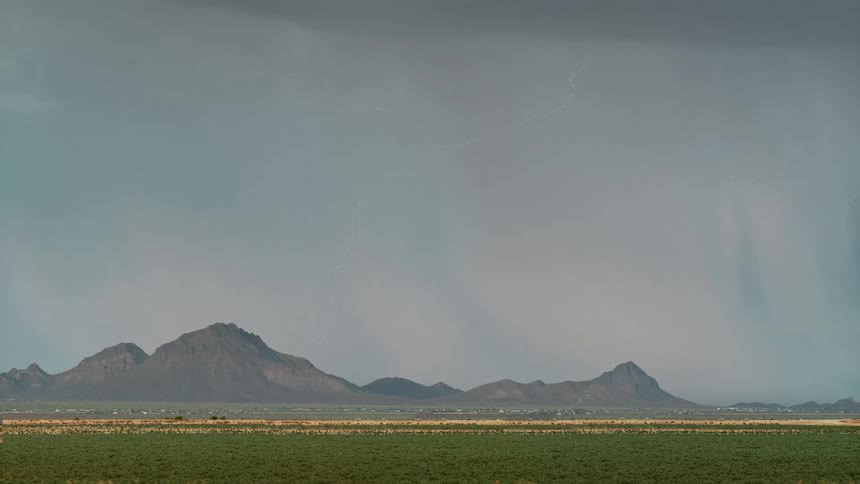 Landscape of a greenish field with mountains on the horizon in a sky with lightning