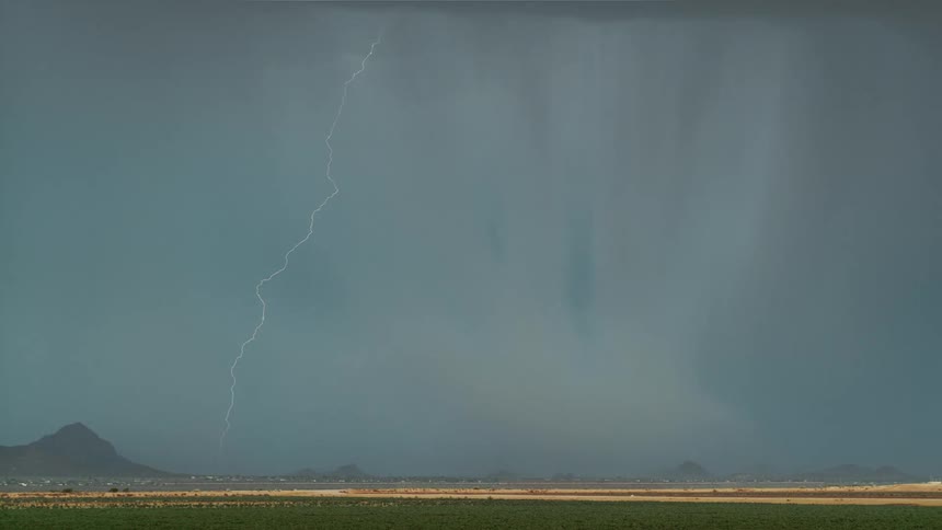 Bright lightning cutting across the sky during a thunderstorm with mountains in the background and a field at the bottom