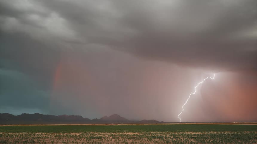 A powerful bolt of lightning strikes down from a stormy sky over a distant mountain range