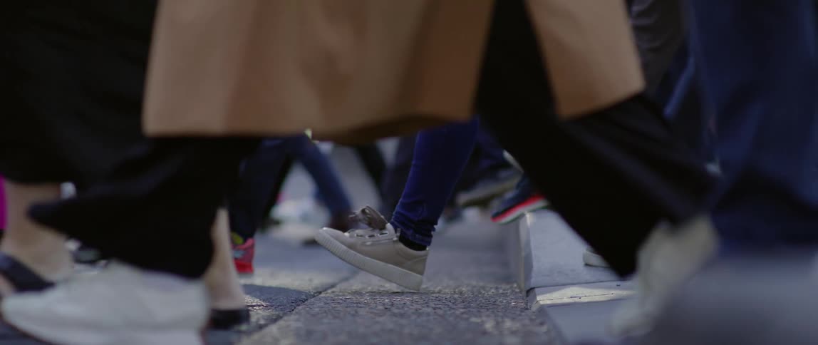 A closeup view of peoples lower legs and feet as they walk on a bustling city street