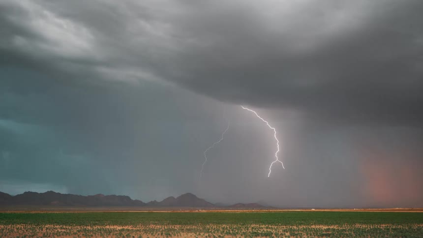Bright lightning cutting across the sky during a thunderstorm with mountains in the background