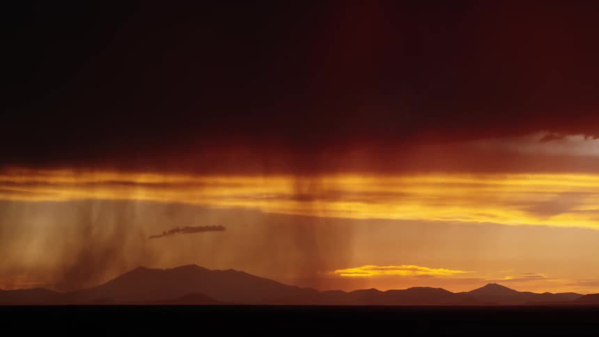 Bright lightning streaking across the sky during a dramatic sunset with dark orange clouds above a silhouette of mountains in the background