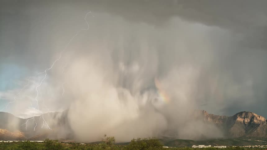 A rainbow forms over a rural area as a storm unleashes lightening