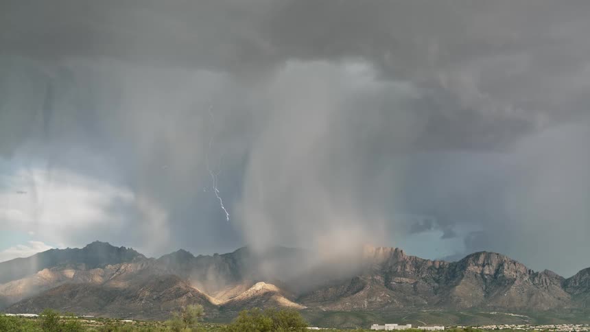 Lightning flashes from gray storm clouds over rocky mountains
