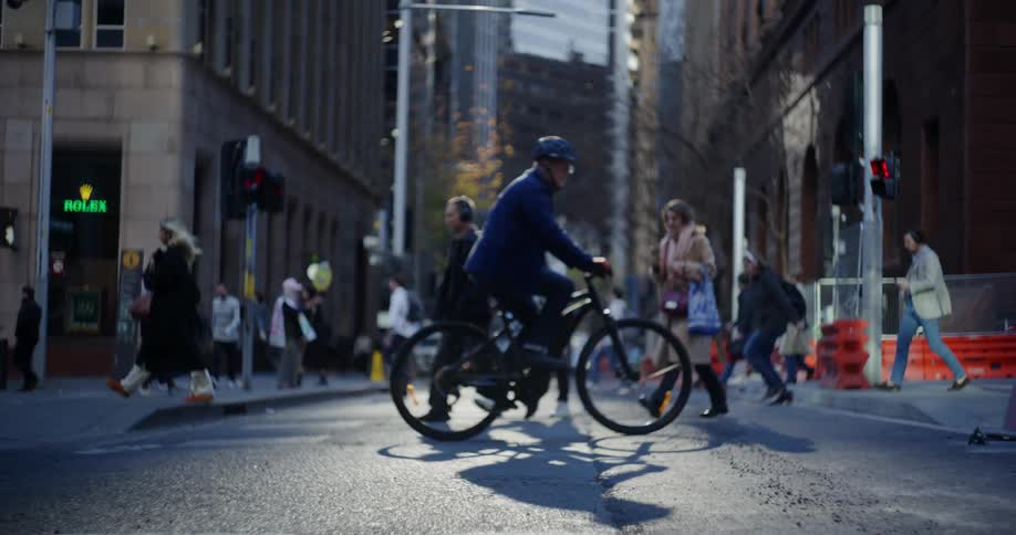 A busy urban street scene with pedestrians crossing the road and a cyclist in the foreground