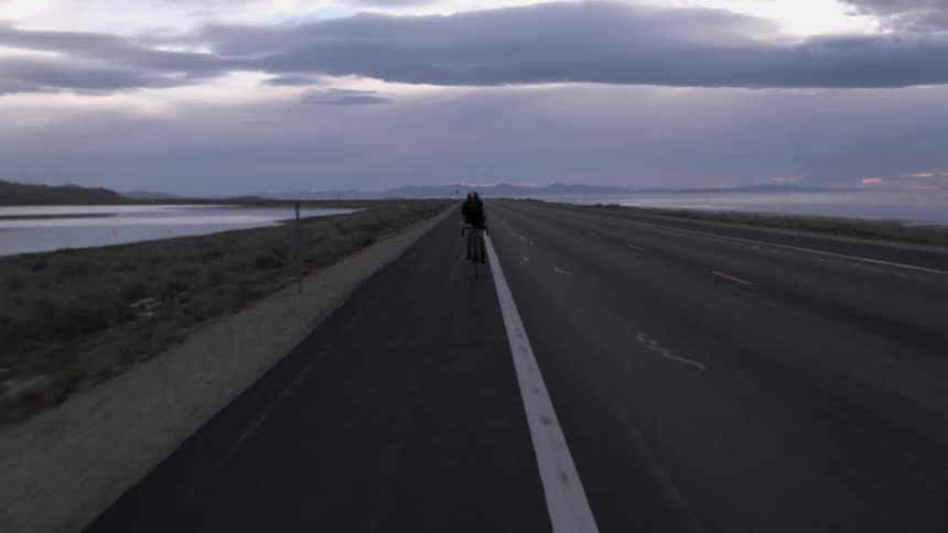 A person is riding a bicycle on a highway at dusk