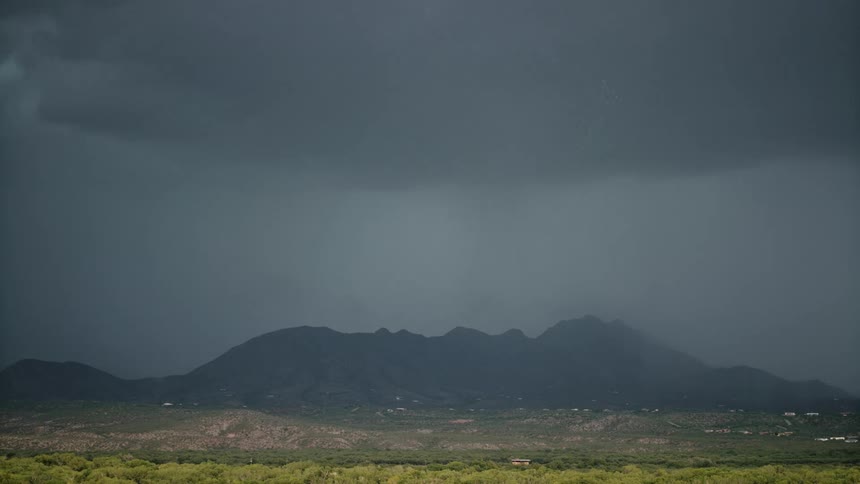 A lightning strike pierces through dark stormy skies illuminating the landscape below