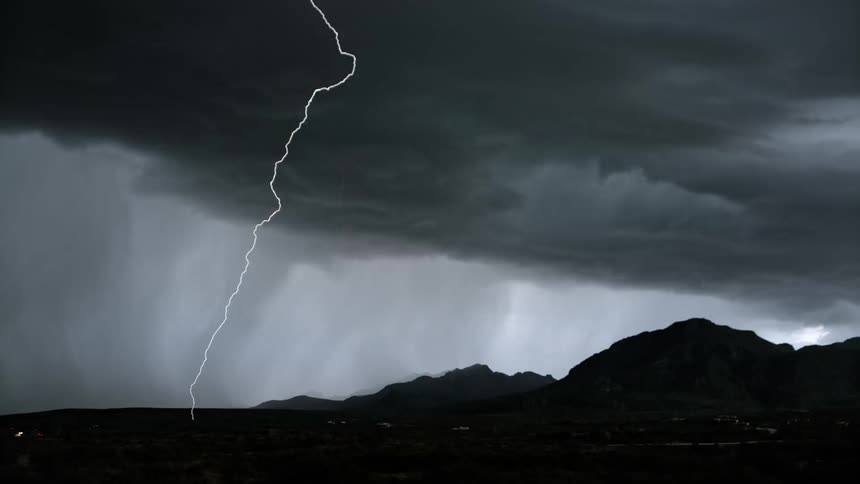 Silhouette of mountains against a rainy sky and lightning