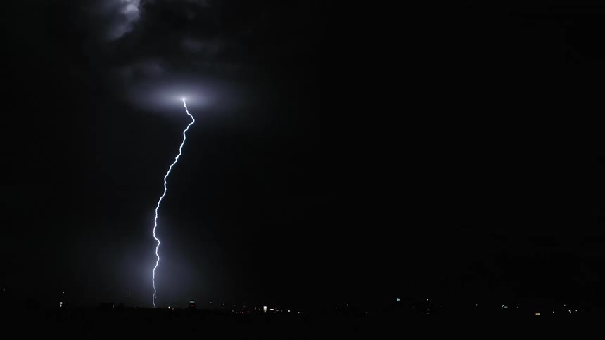 A night sky with several striking lightning bolts illuminating the clouds a city skyline in the background