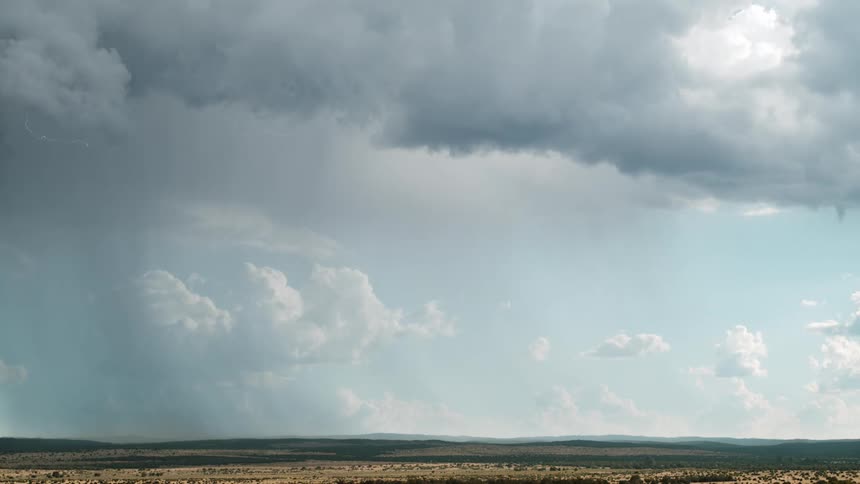 Rain falls from storm clouds lit up with lightening over hills and plains