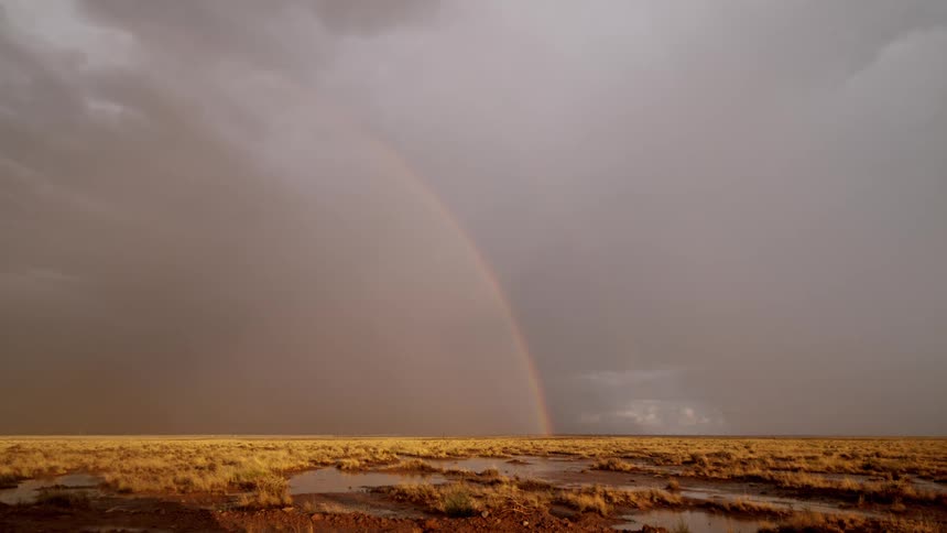 Field with bodies of water and on the horizon in the rainbow in a storm
